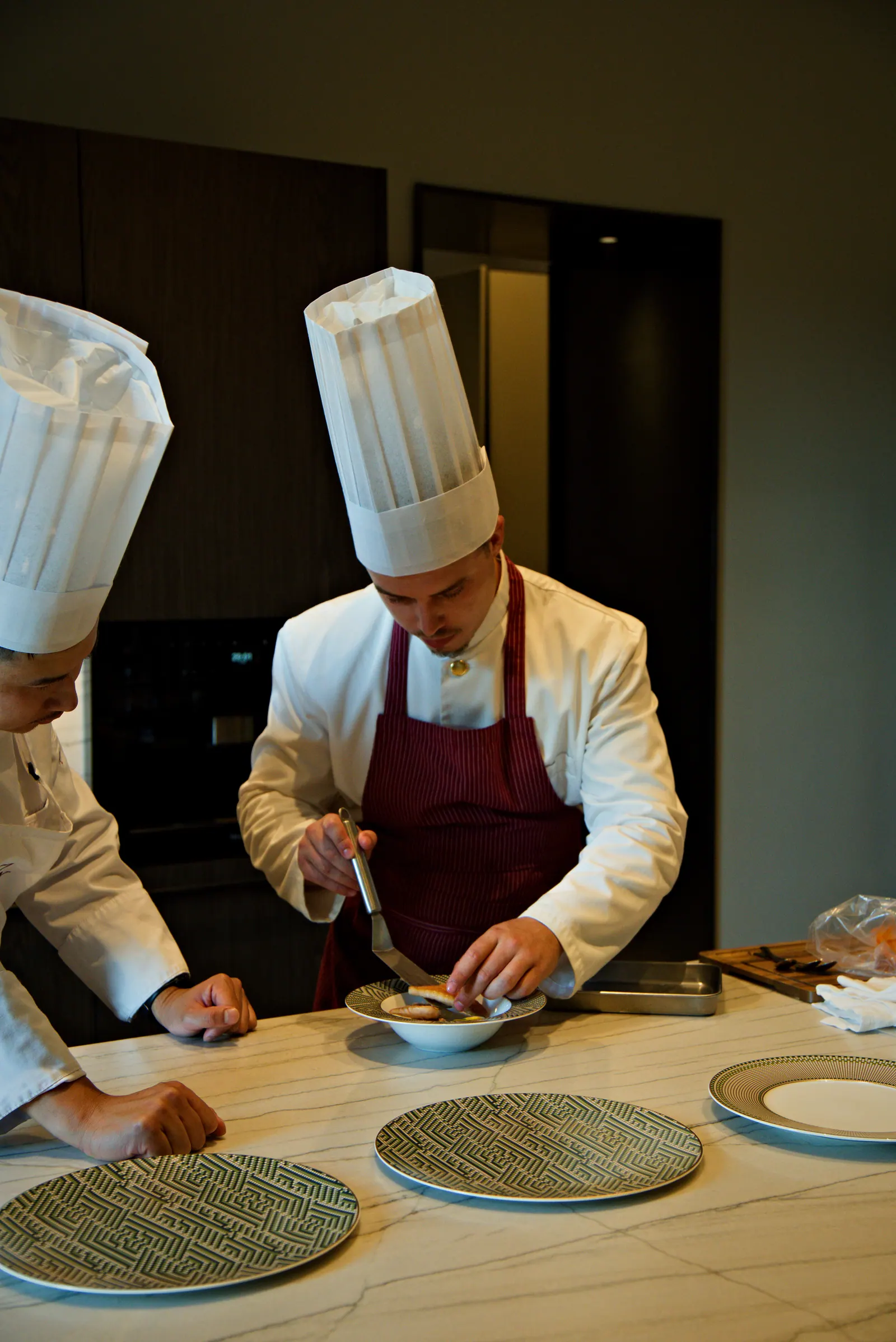 Le chef Sean en tablier bordeaux dresse un plat en action pendant le service