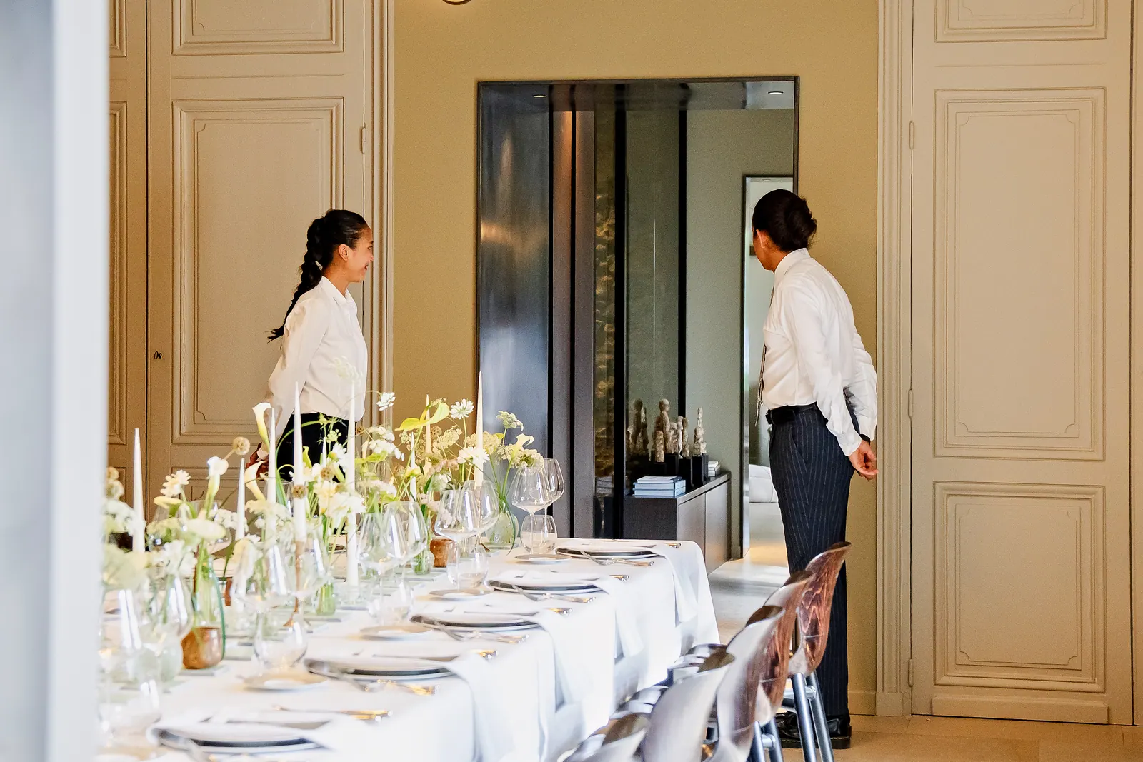 Longue table dressée de fleurs blanches, bougies et verrerie fine dans le salon d'un château, pour un événement privé